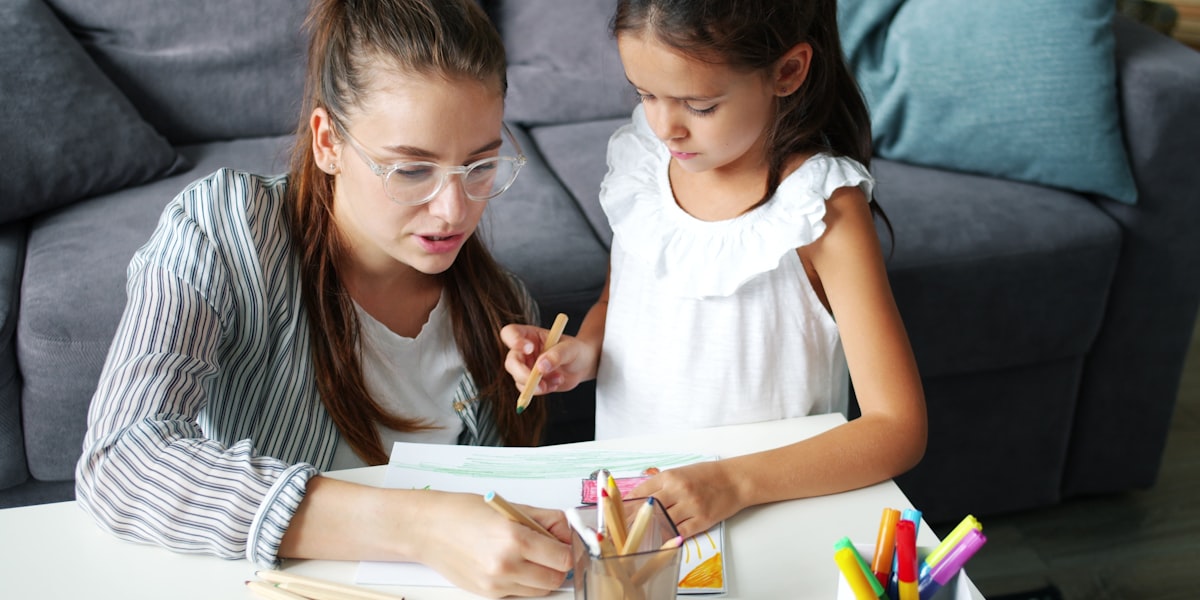 An older teen helping a younger child with homework at a table